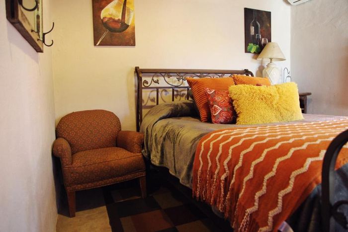 Habitación acogedora con cama de hierro forjado, ropa de cama naranja y sillón marrón junto a la pared.