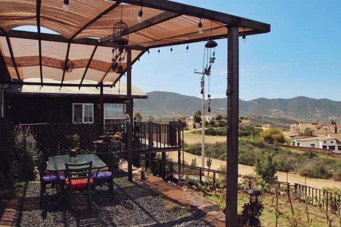 Patio con mesa y sillas bajo una pérgola, con vistas a un soleado paisaje rural y a las colinas lejanas.