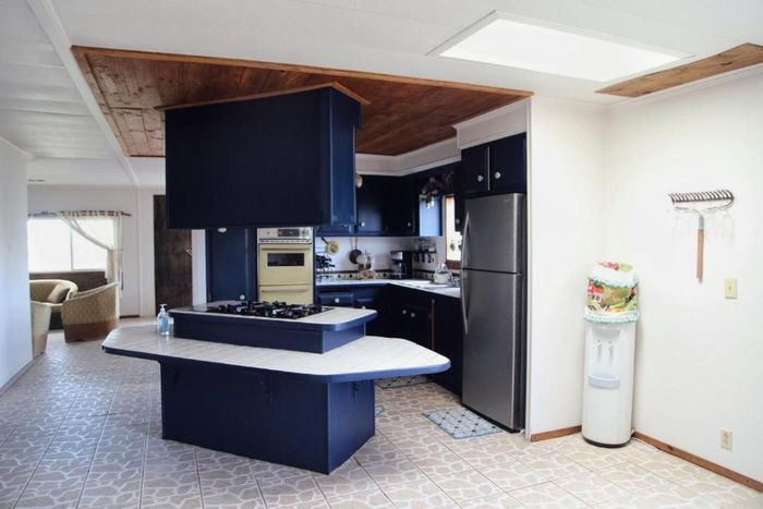 Cocina vacía con armarios azul oscuro, encimeras blancas y una isla central bajo un techo revestido de paneles de madera.