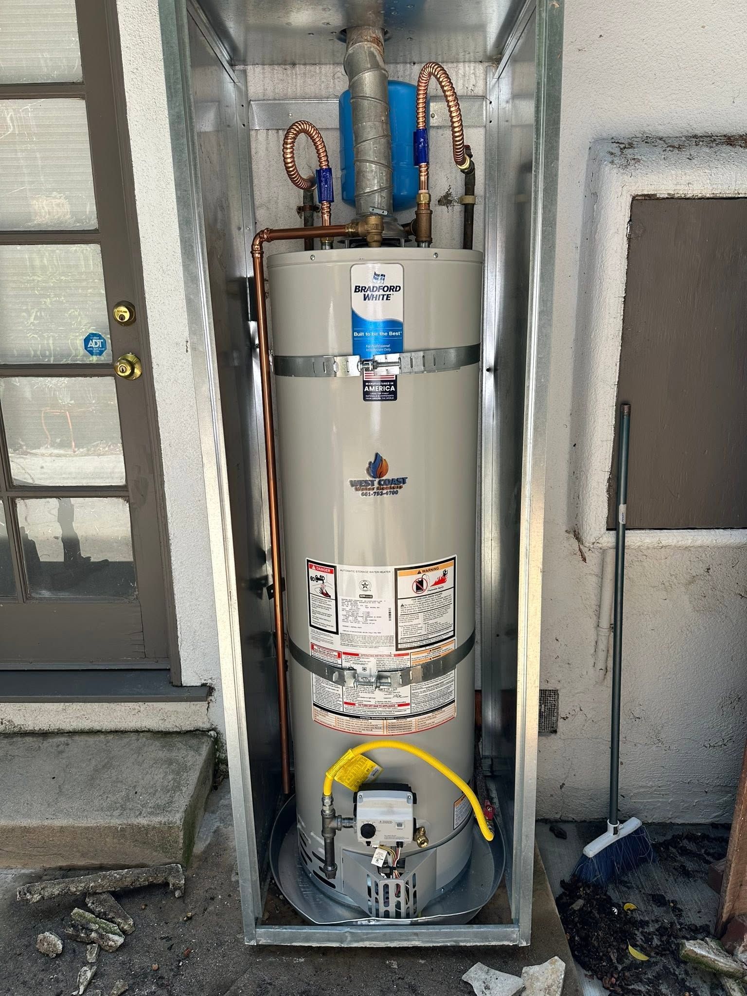 Water heater in a utility alcove with exposed pipes and a control panel at the bottom.