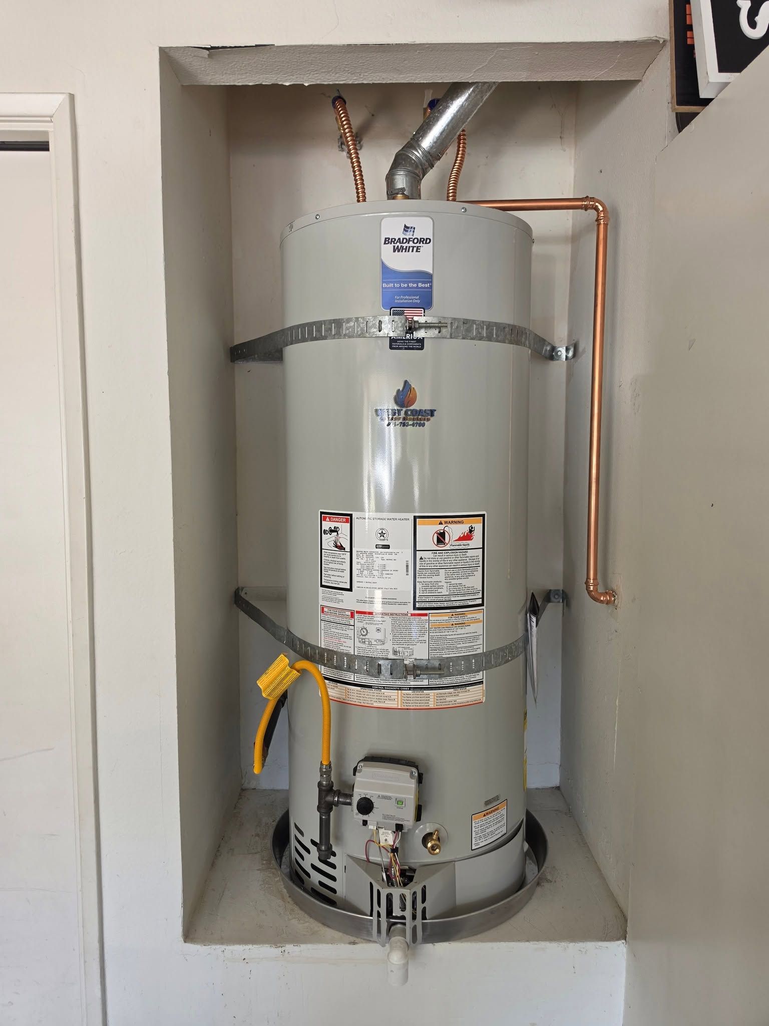 Water heater in a utility closet with exposed copper pipes and fittings.