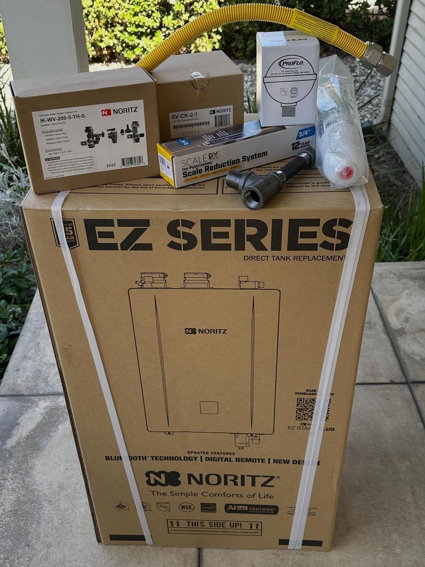 Cardboard Noritz EZ Series water heater box with accessories and a white bag on top outdoors