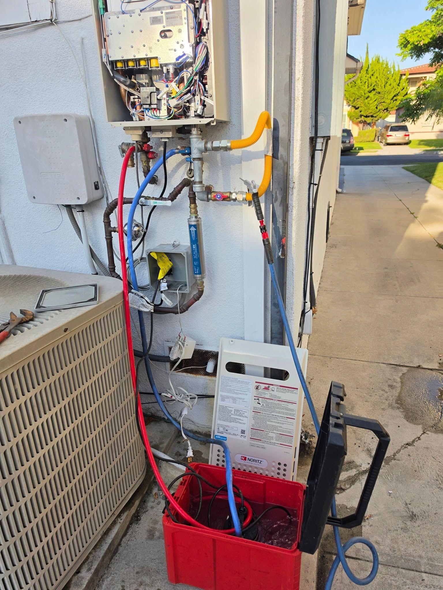Electrical panels, wires, and a red bucket beside a building wall outdoors.