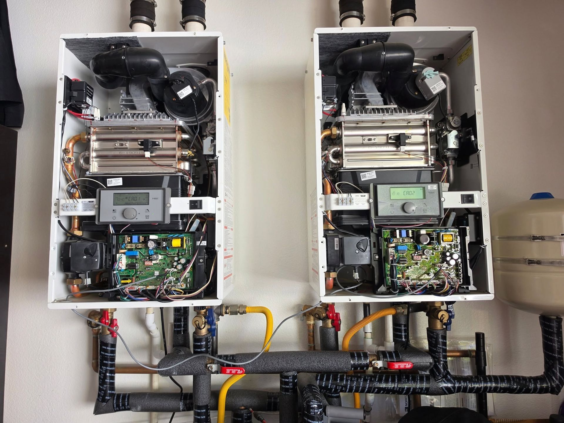 Two open electrical control cabinets with wiring, circuit boards, and fans mounted on a wall.