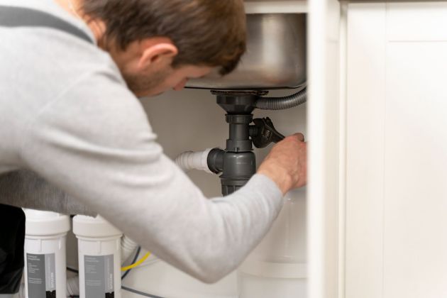 Plumber repairing a sink drain under a bathroom cabinet
