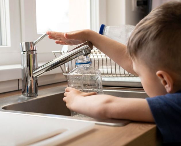 Child reaching for running water at a kitchen sink with a glass under the faucet