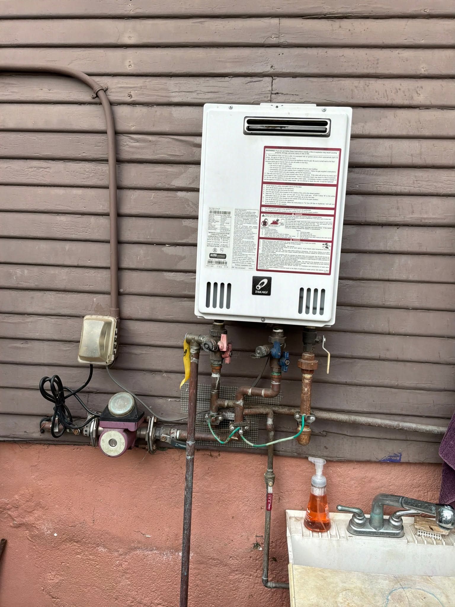 Gas water heater and outdoor utility meters mounted on a wall with exposed pipes and valves.
