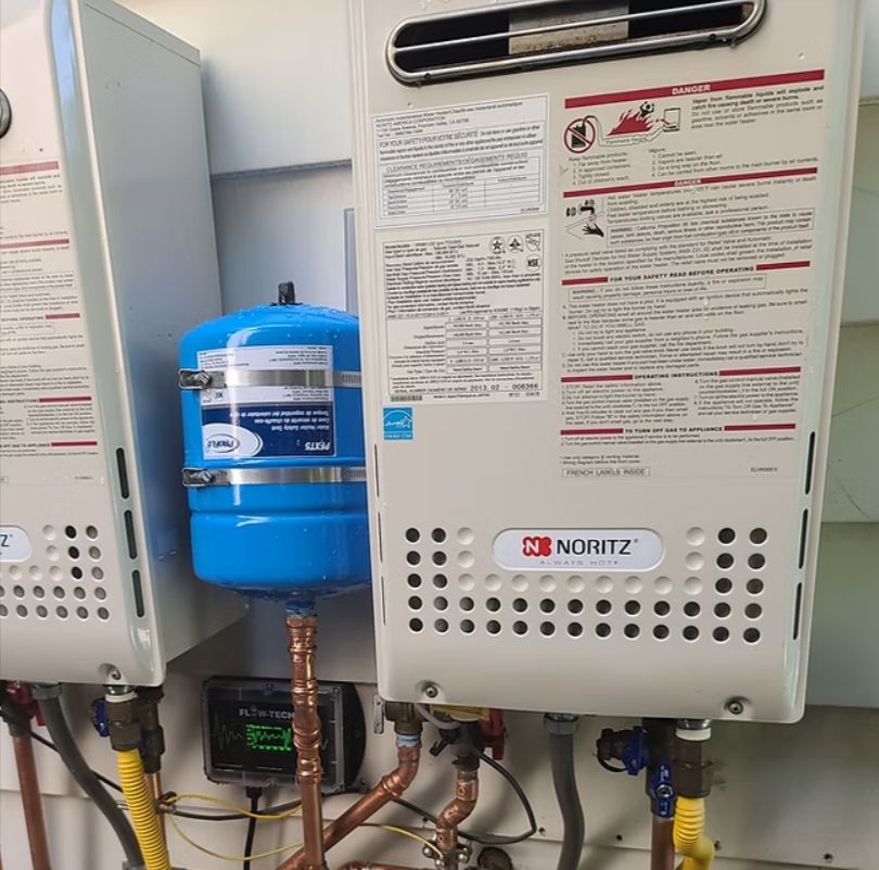 Wall-mounted Noritz water heaters with blue expansion tank and exposed plumbing in a utility room