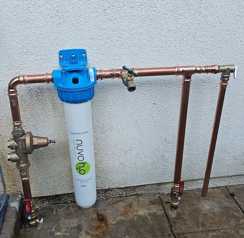 Blue water filter mounted on copper pipes against a stucco wall.