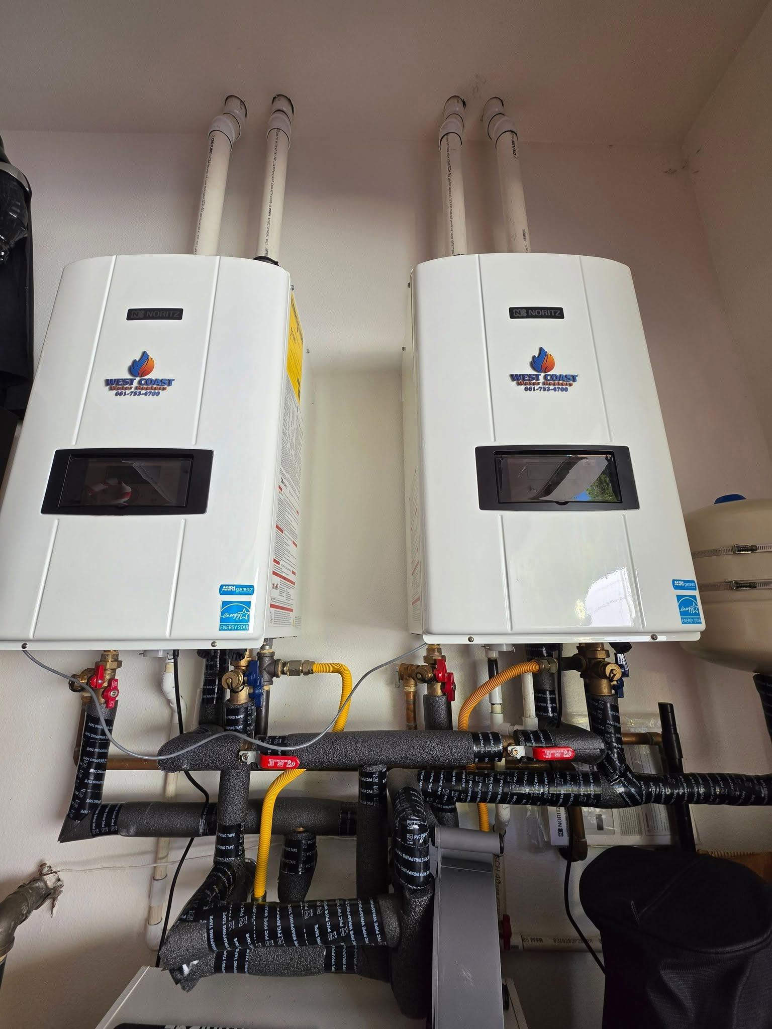 Two white wall-mounted boilers with black vents and pipes in a utility room.
