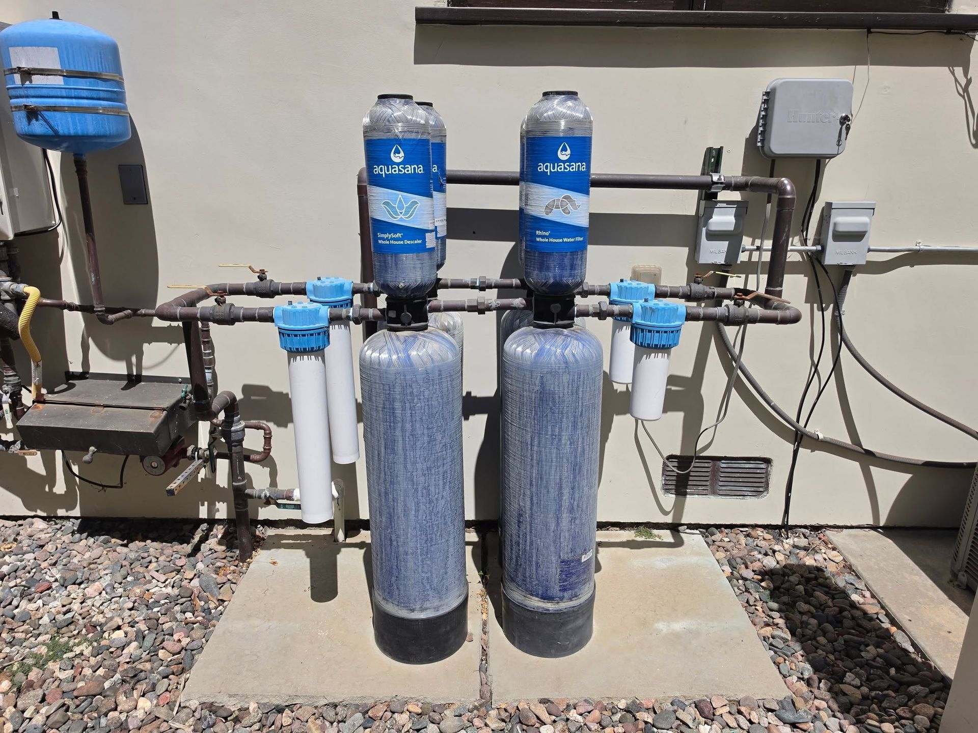 Two blue water filtration tanks and pipes mounted outdoors beside a building.