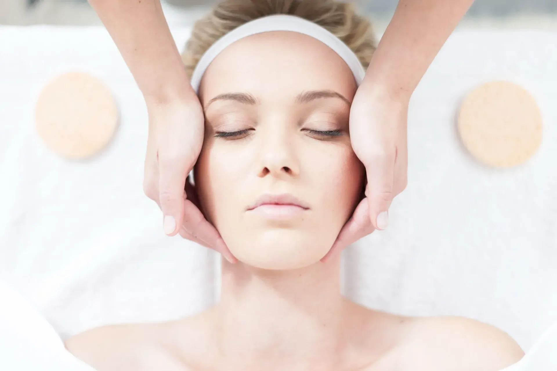 Behandschuhte Hände wenden ein rotes Gesichtsbehandlungsgerät an einer Frau an, die auf einer Spa-Liege liegt.