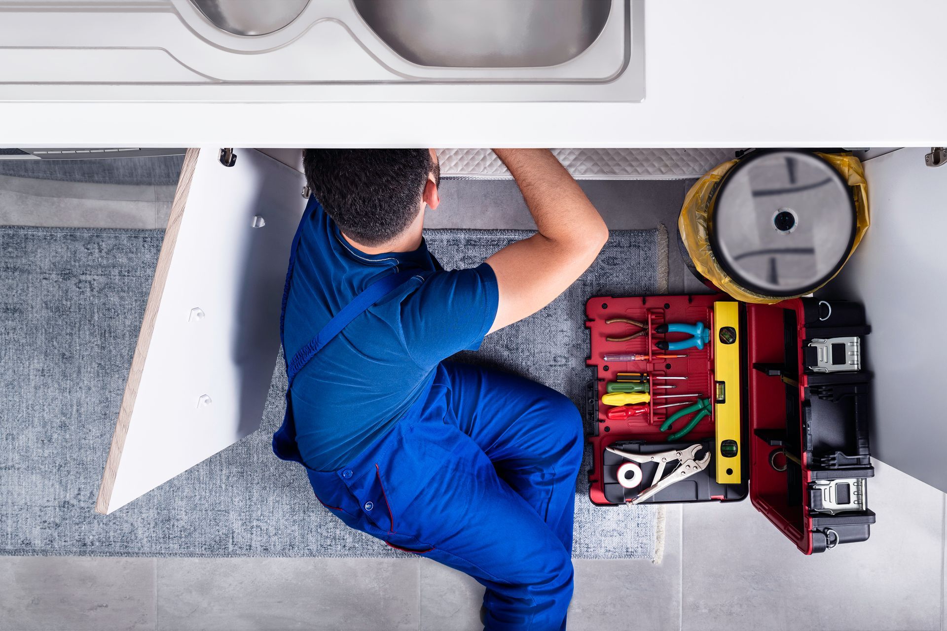 A plumber is working under a sink in a kitchen. A plumber is working under a sink in a kitchen.