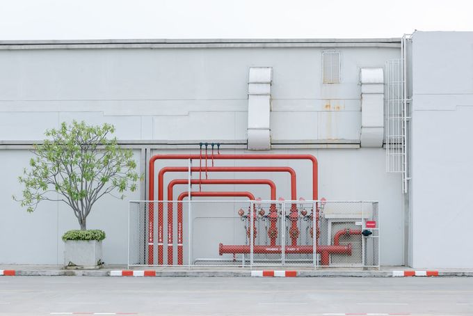 A white building with red pipes and a tree in front of it. A white building with red pipes and a tree in front of it.