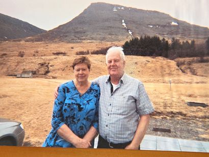 Two people standing outdoors before a mountain and rocky hillside, smiling at the camera.