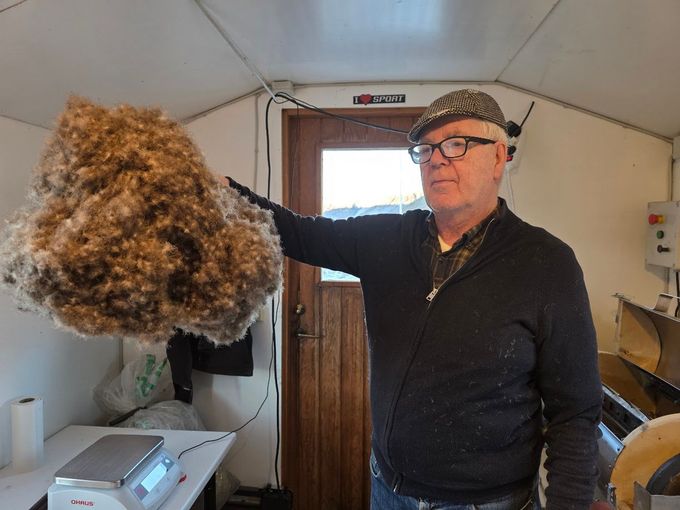 Man holding a large clump of eiderdown or inside a small room, with equipment in the background