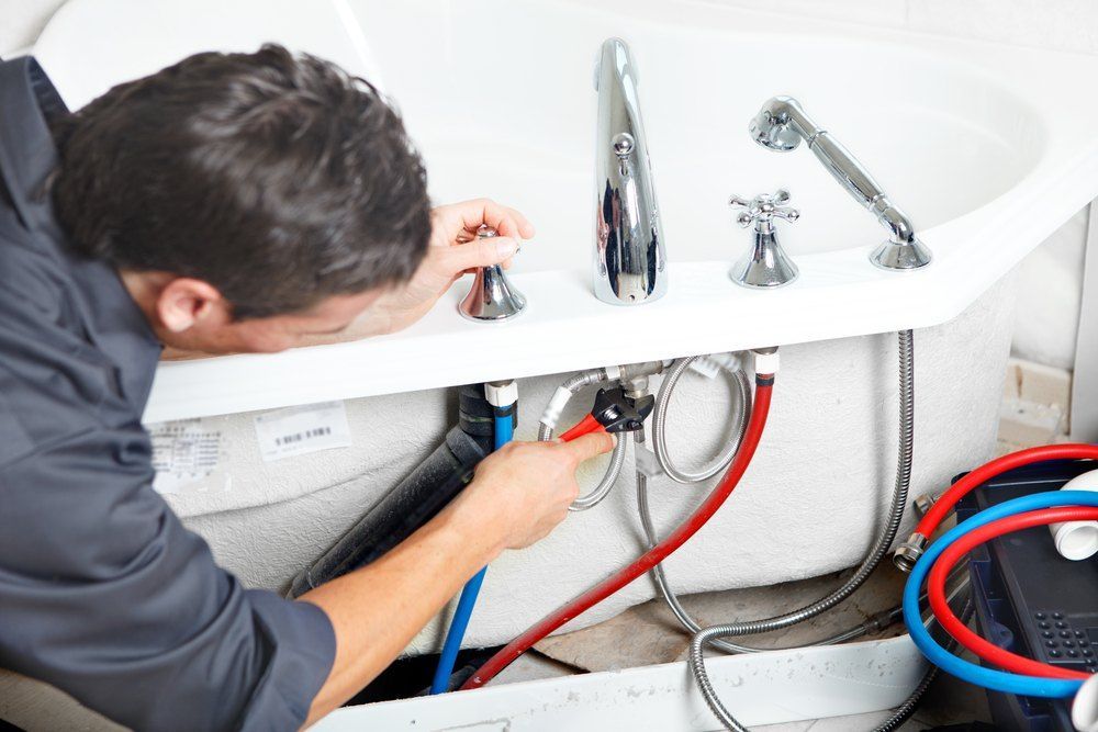 A Man is Fixing a Bathtub With a Wrench — Tony Brown Plumbing & Gas Services in South Grafton, NSW