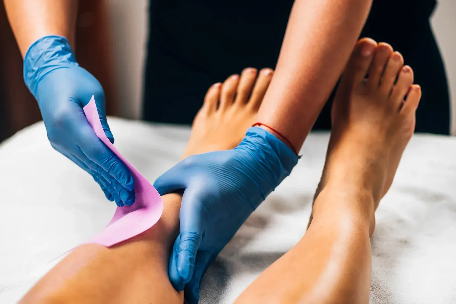 A woman is getting her feet waxed by a woman wearing blue gloves.