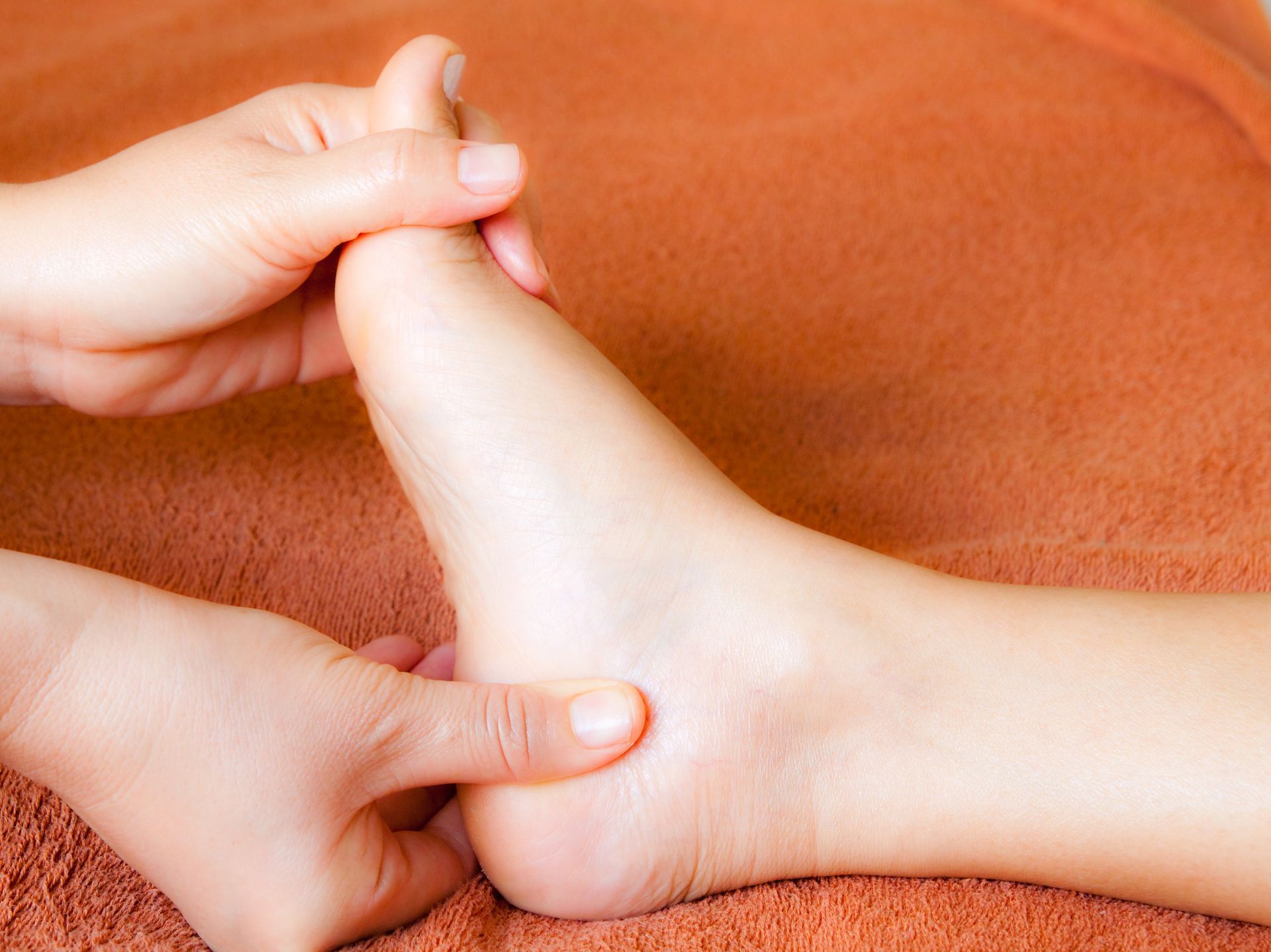 Hands massaging a foot on a brown towel; the focus is on the ankle and heel.