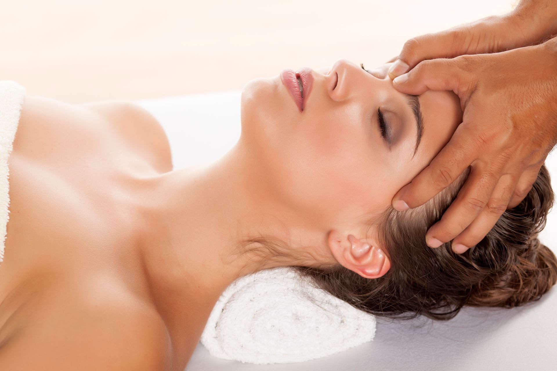 Woman receiving a head massage; white towel under her head; hands on her forehead.