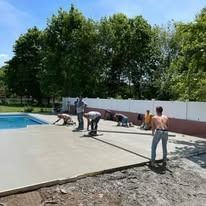 A group of people are working on a concrete deck next to a swimming pool.
