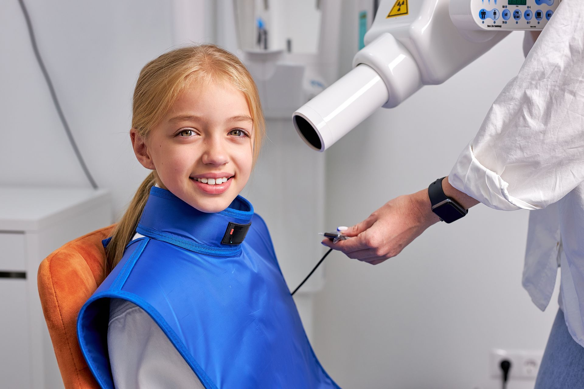 A little girl is sitting in a dental chair getting an x-ray of her teeth.