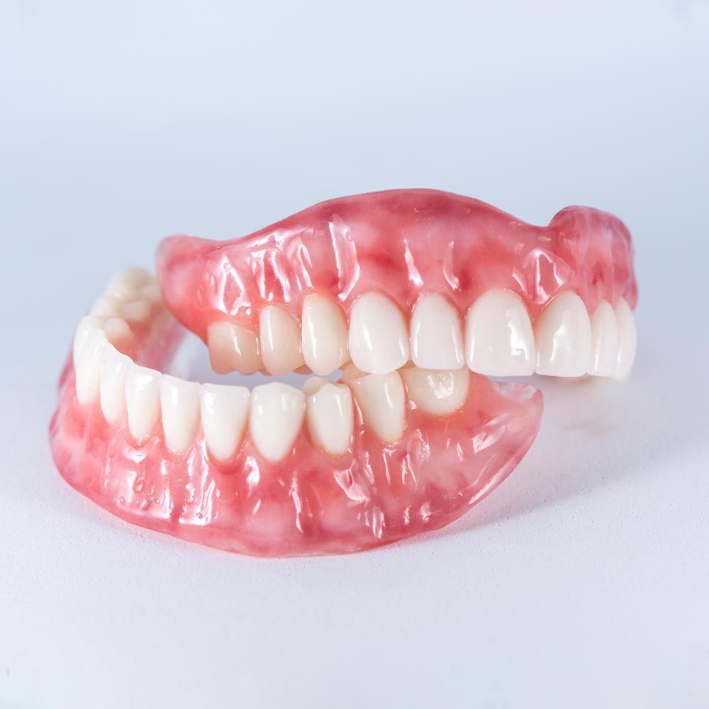 A close up of a denture with white teeth on a white surface.