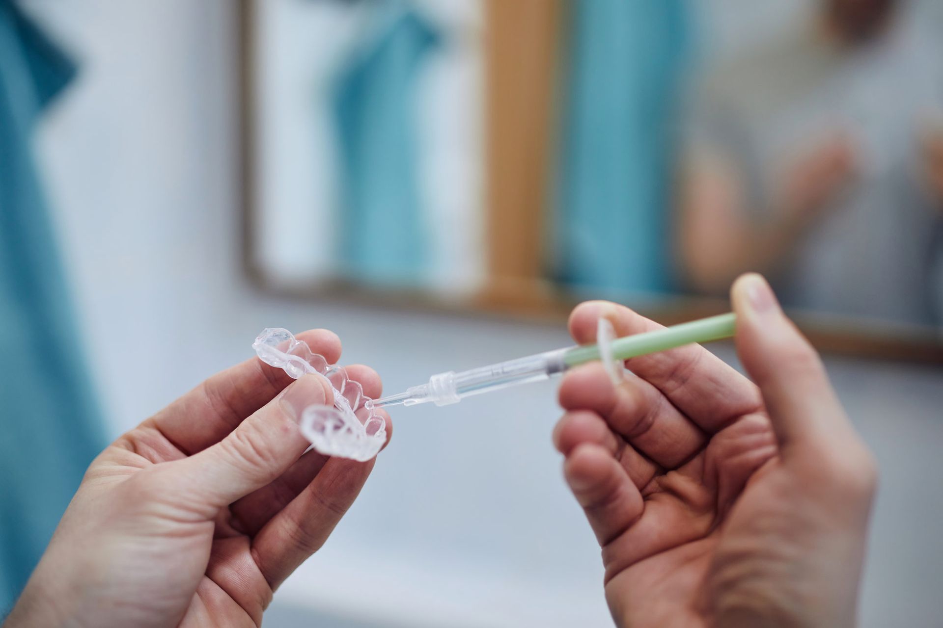 A person is holding a syringe and a tooth whitening kit in their hands.