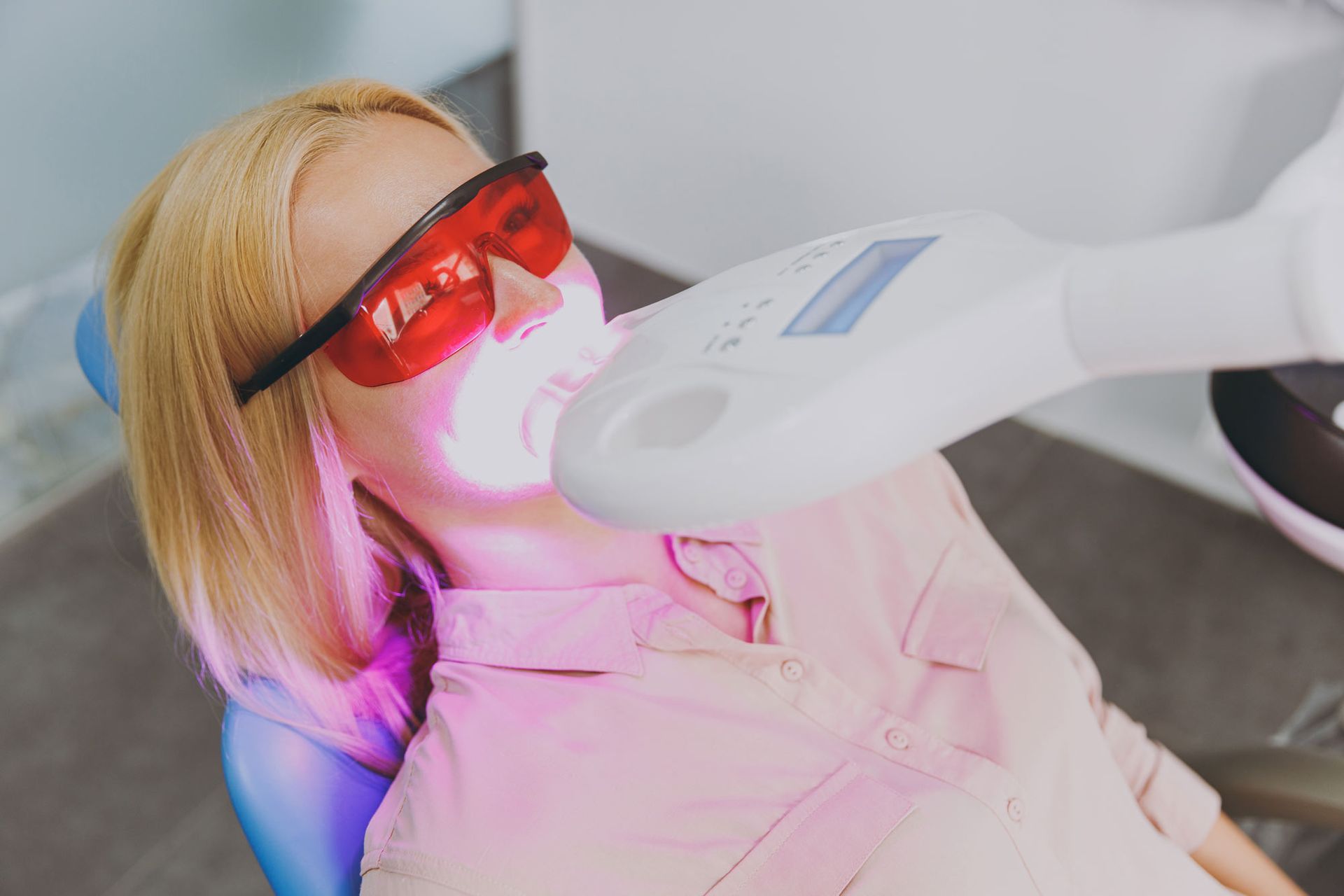 A woman is getting her teeth whitened in a dental office.