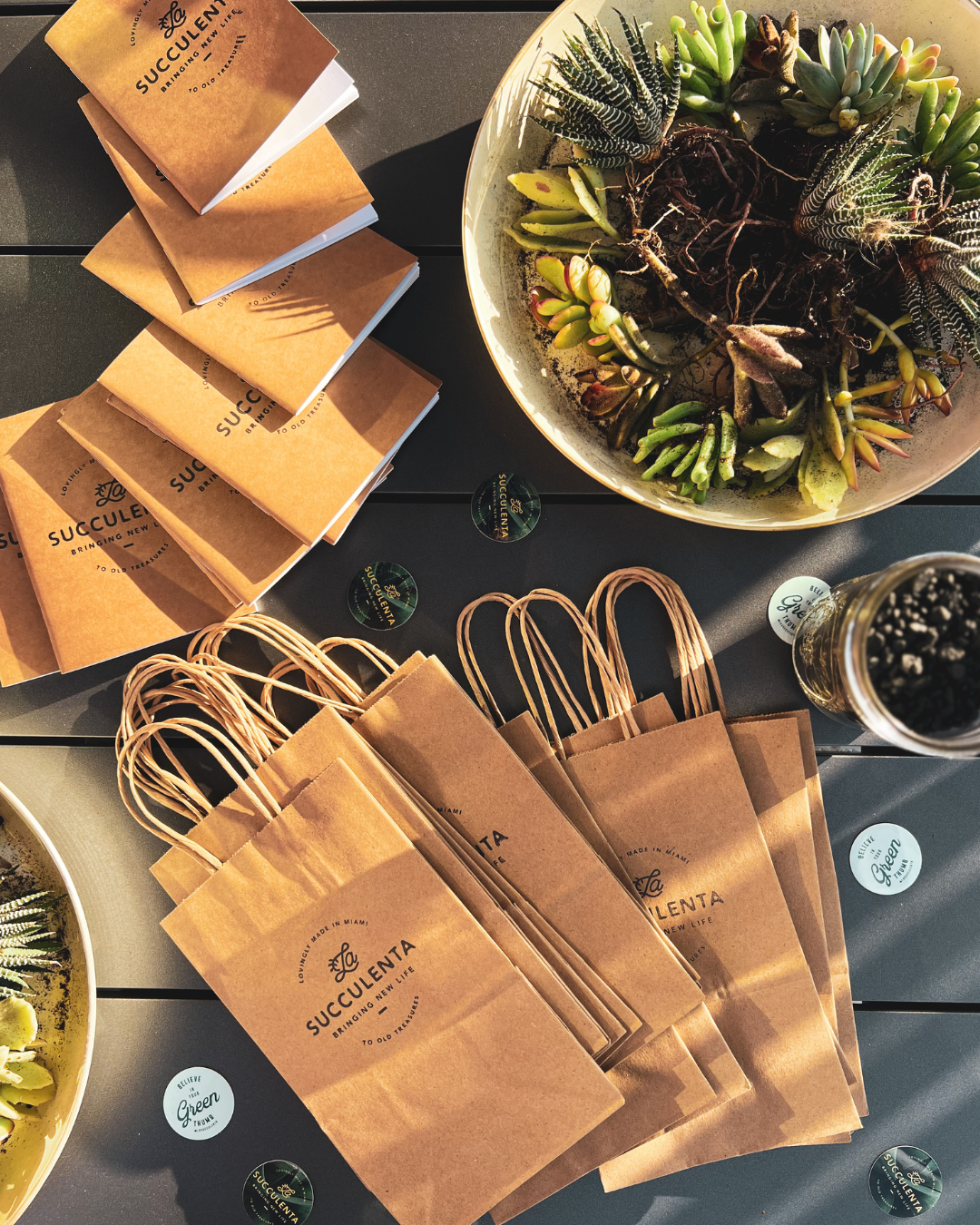 Brown paper bags and boxes arranged with potted succulent centerpieces on a dark table.