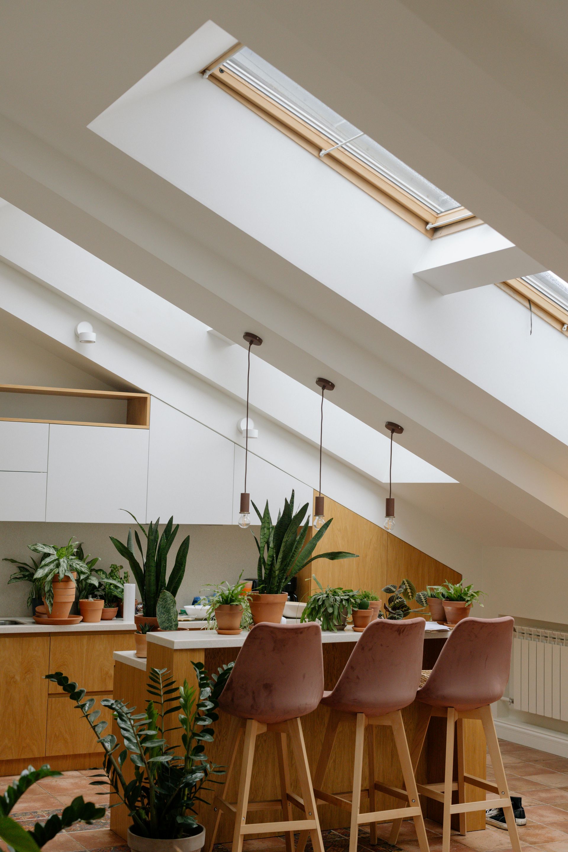 Bright loft kitchen with skylights, wooden stools, and potted plants by a counter
