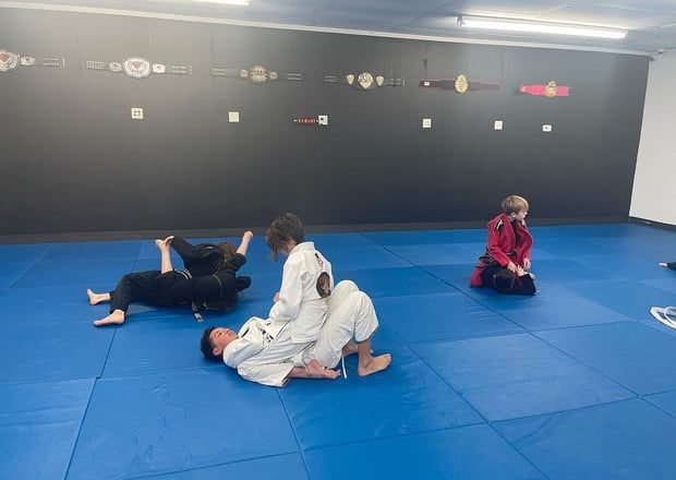 People in martial arts training on a blue mat, indoors.