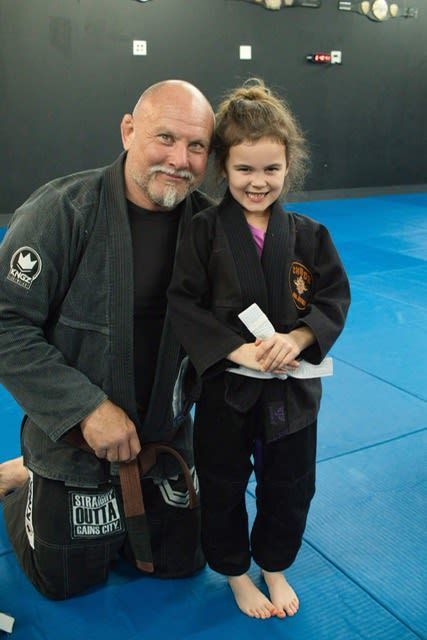 Man in black gi kneels next to young girl in a black gi.