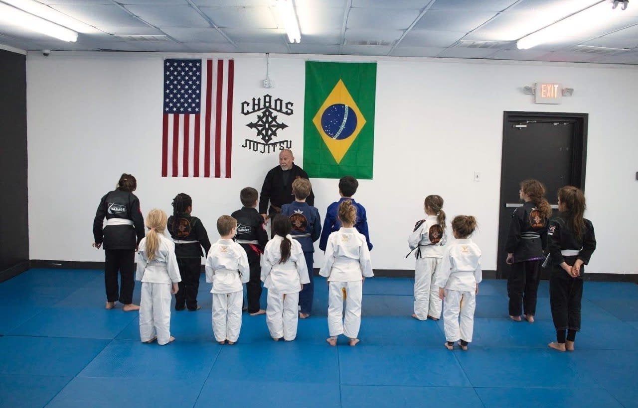 Children in martial arts uniforms stand facing a man.