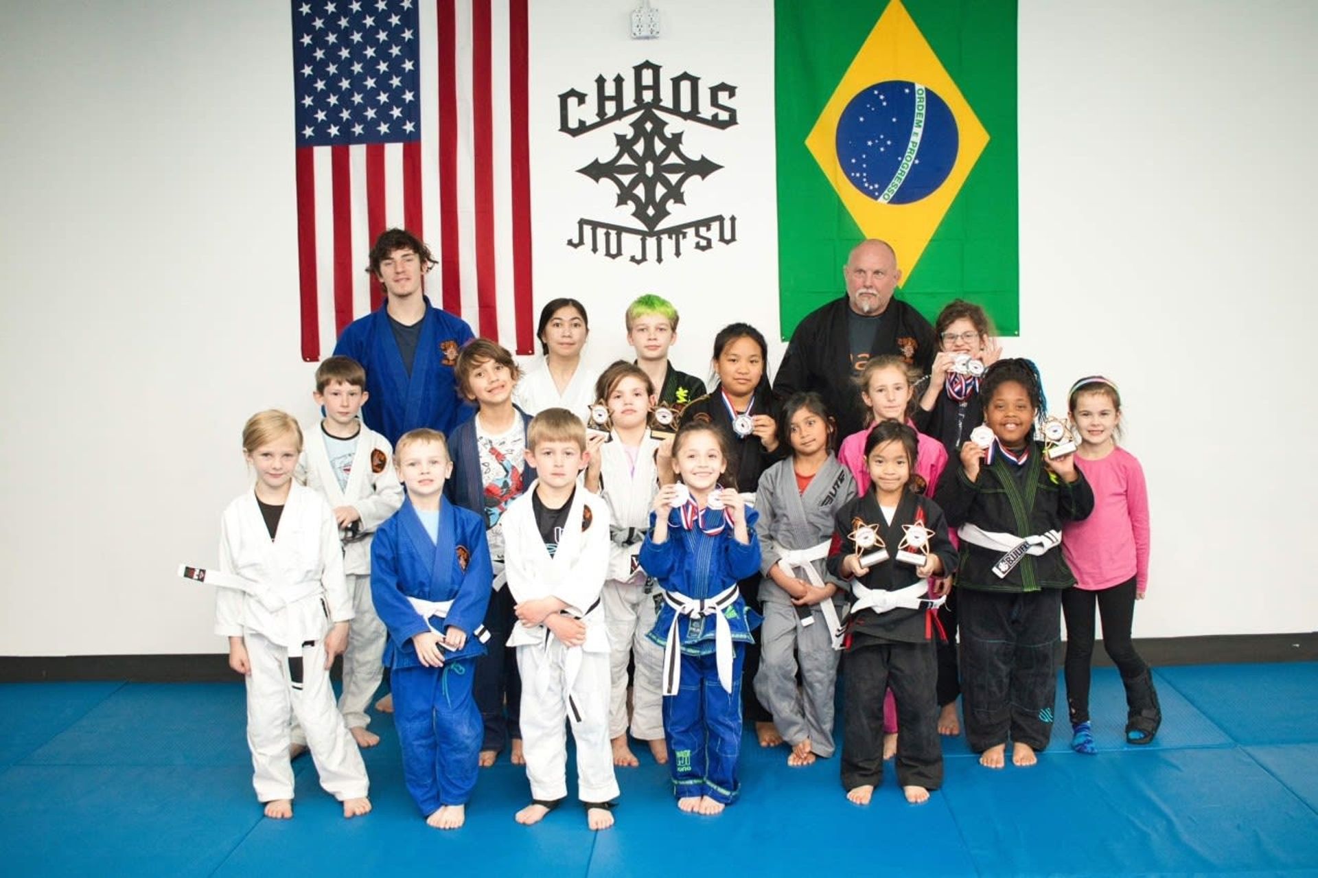 Group of children in martial arts uniforms posing for a photo in a dojo with flags.