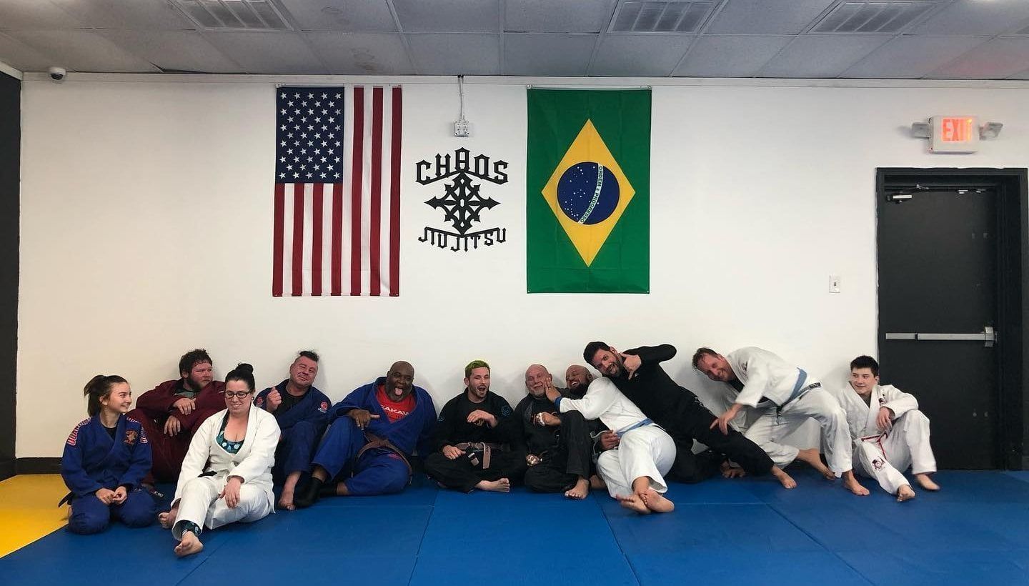 Group of people in martial arts attire sitting on a blue mat.