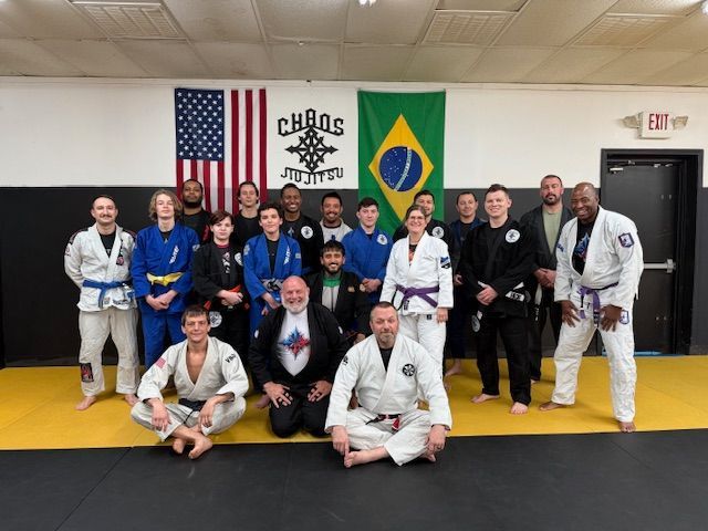 A group posing in a martial arts gym with American and Brazilian flags on the wall and a black and yellow mat.