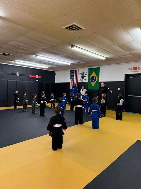 A group of students in martial arts uniforms practicing in a gym with American and Brazilian flags on the wall.