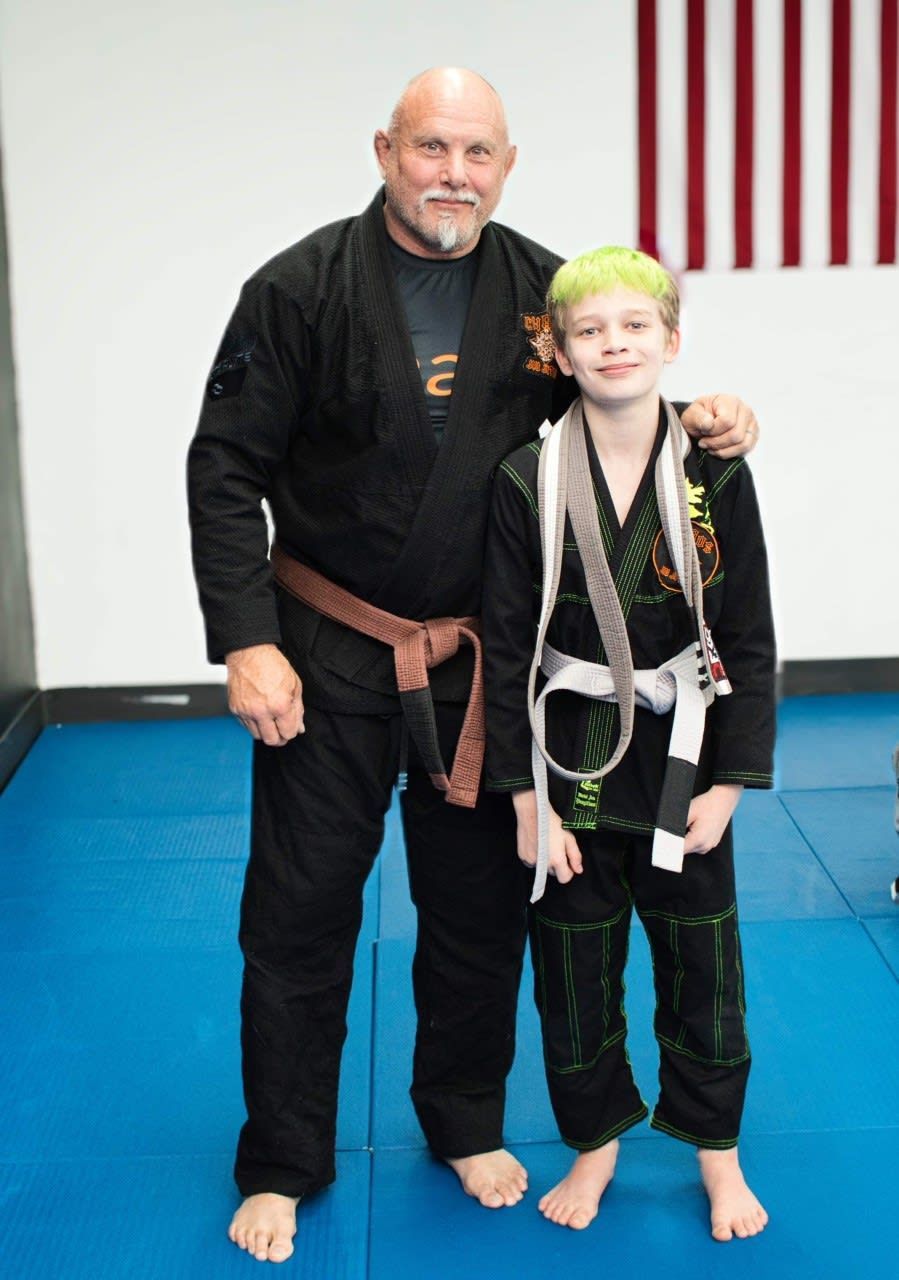 Man with brown belt and boy with white belt in martial arts uniforms on a blue mat.