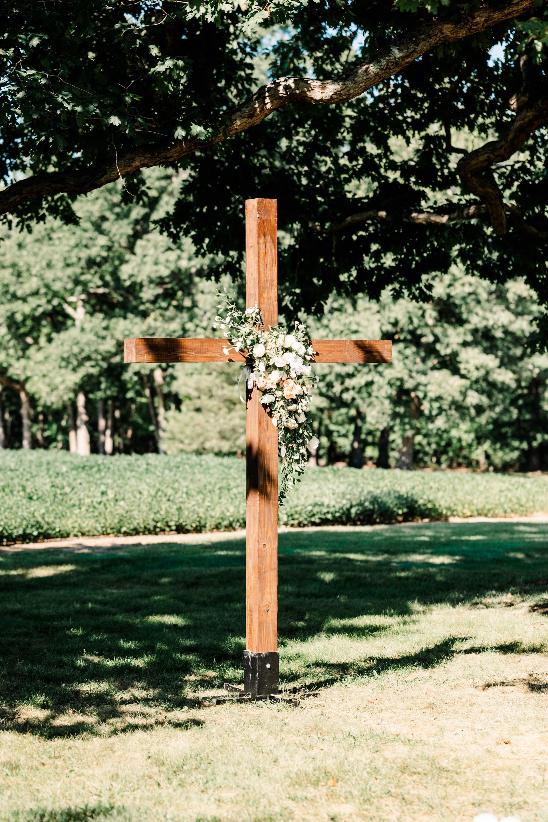 A wooden cross is sitting in the grass under a tree.