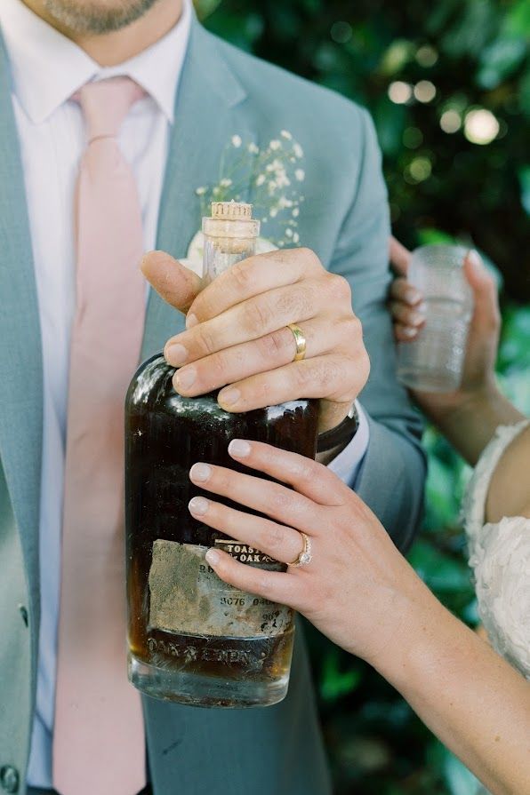 A man in a suit and tie is holding a bottle of whiskey.