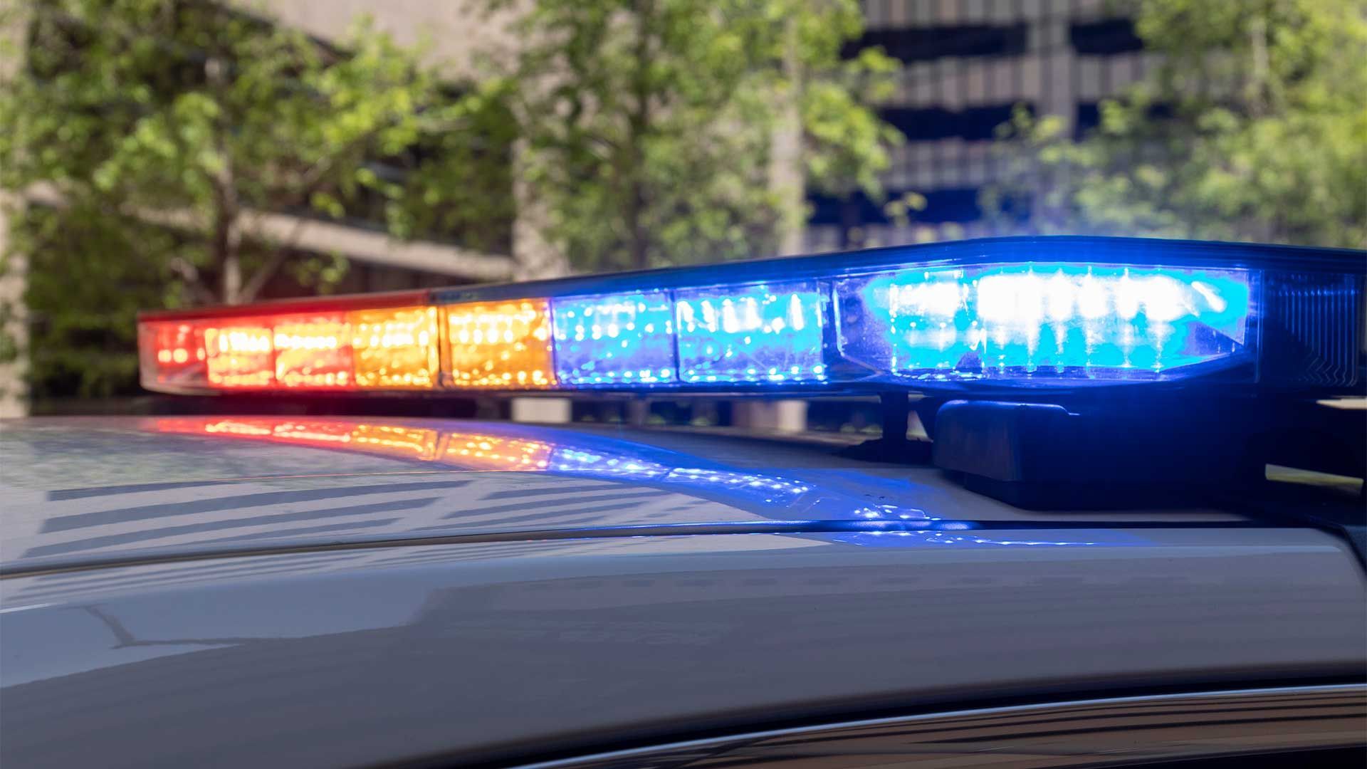 Police car with flashing red and blue lights; background of trees and building.
