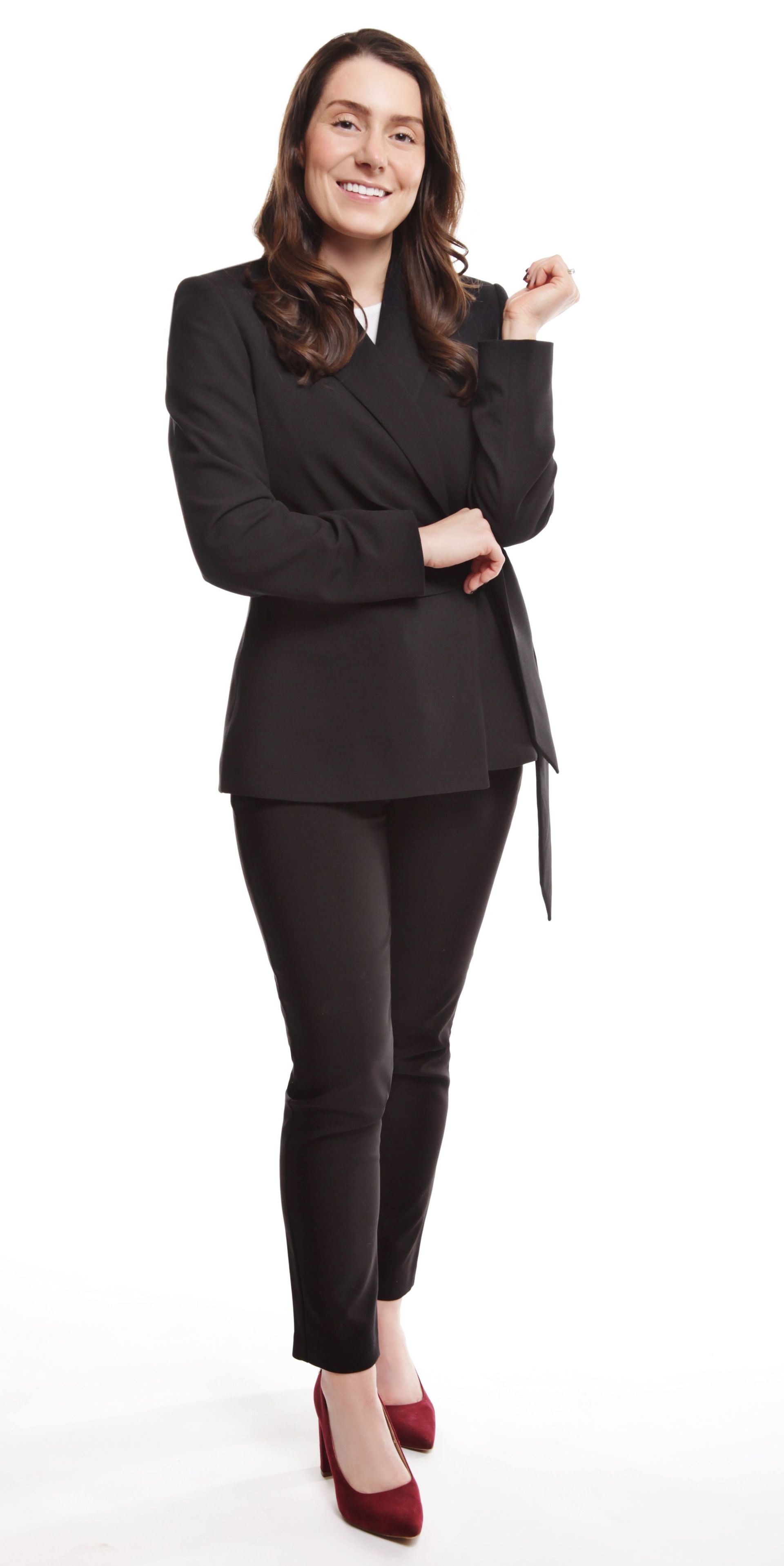 Woman in black suit and pants smiles, posed with arm up, red heels.