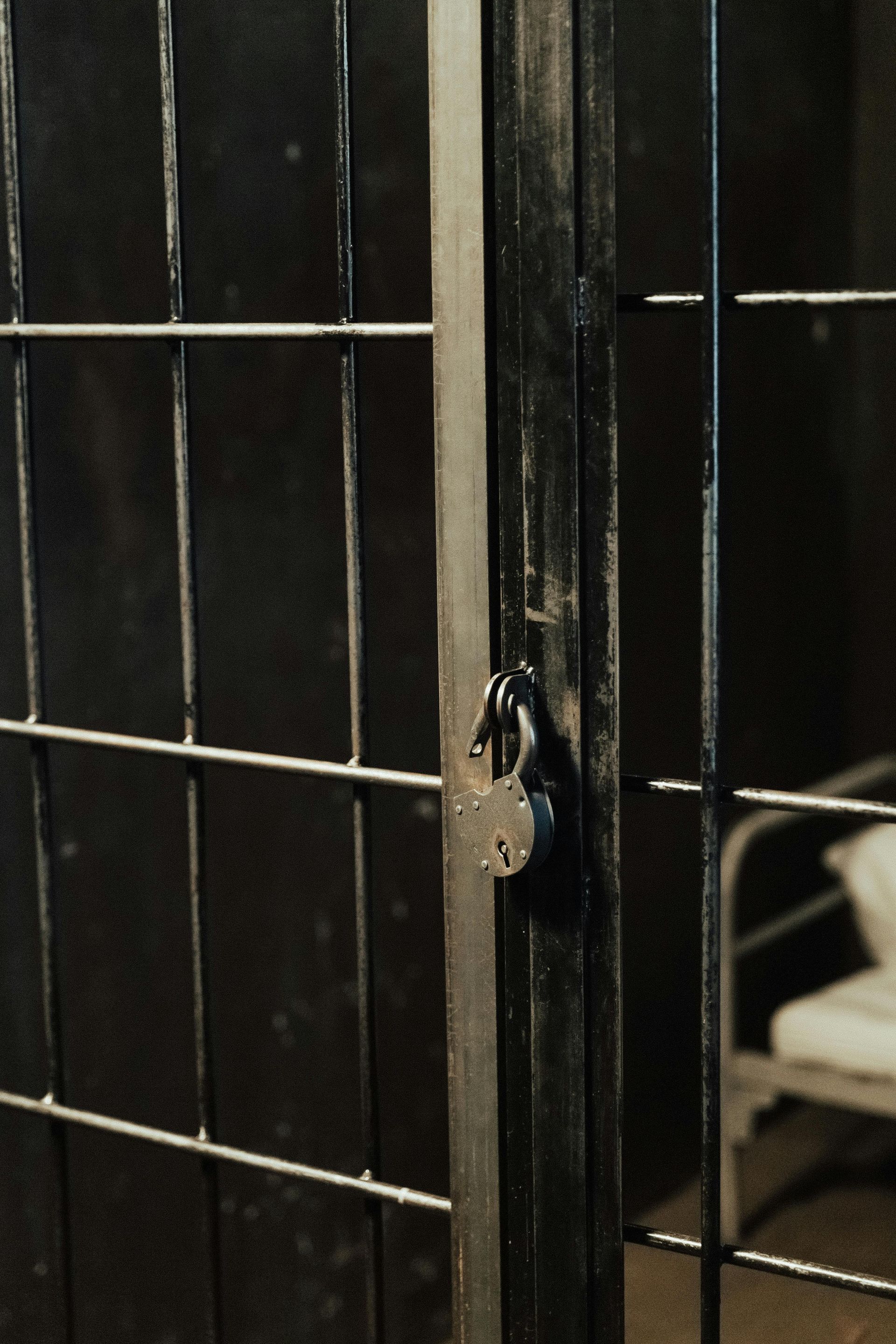 A rusty black metal cage door with a padlock, in a dimly lit room.