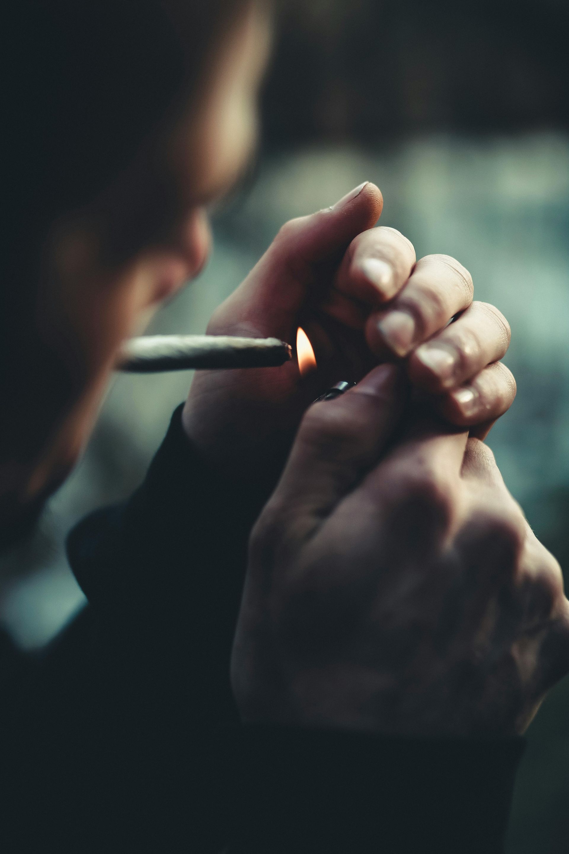 Person lighting a cigar with a lighter; close-up of hands and face in dim light.