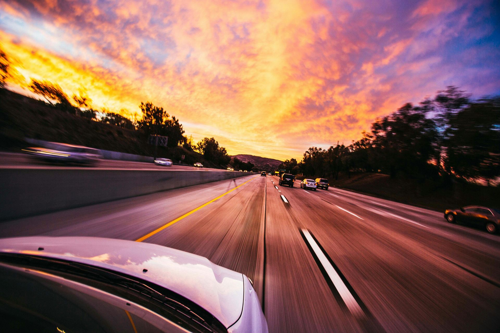 Cars driving on highway under a vibrant, orange and purple sunset.