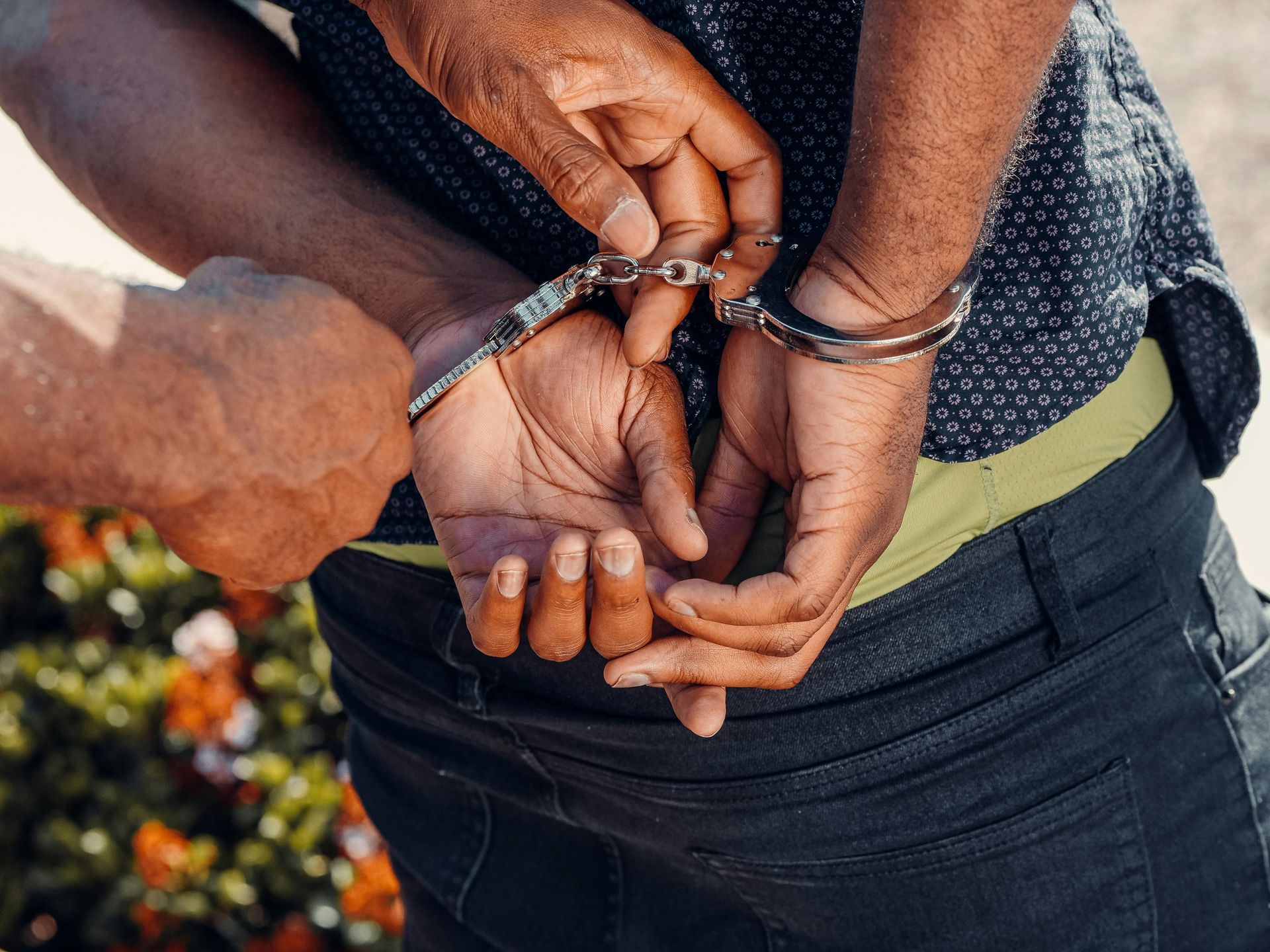 Person's hands being cuffed by another's hand. Focus is on hands and handcuffs.