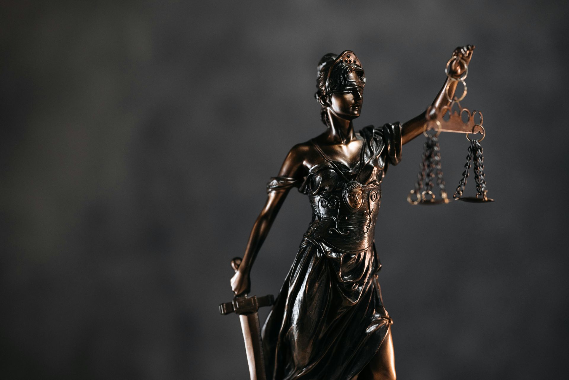 Statue of Lady Justice holding scales and sword, set against a gray background.