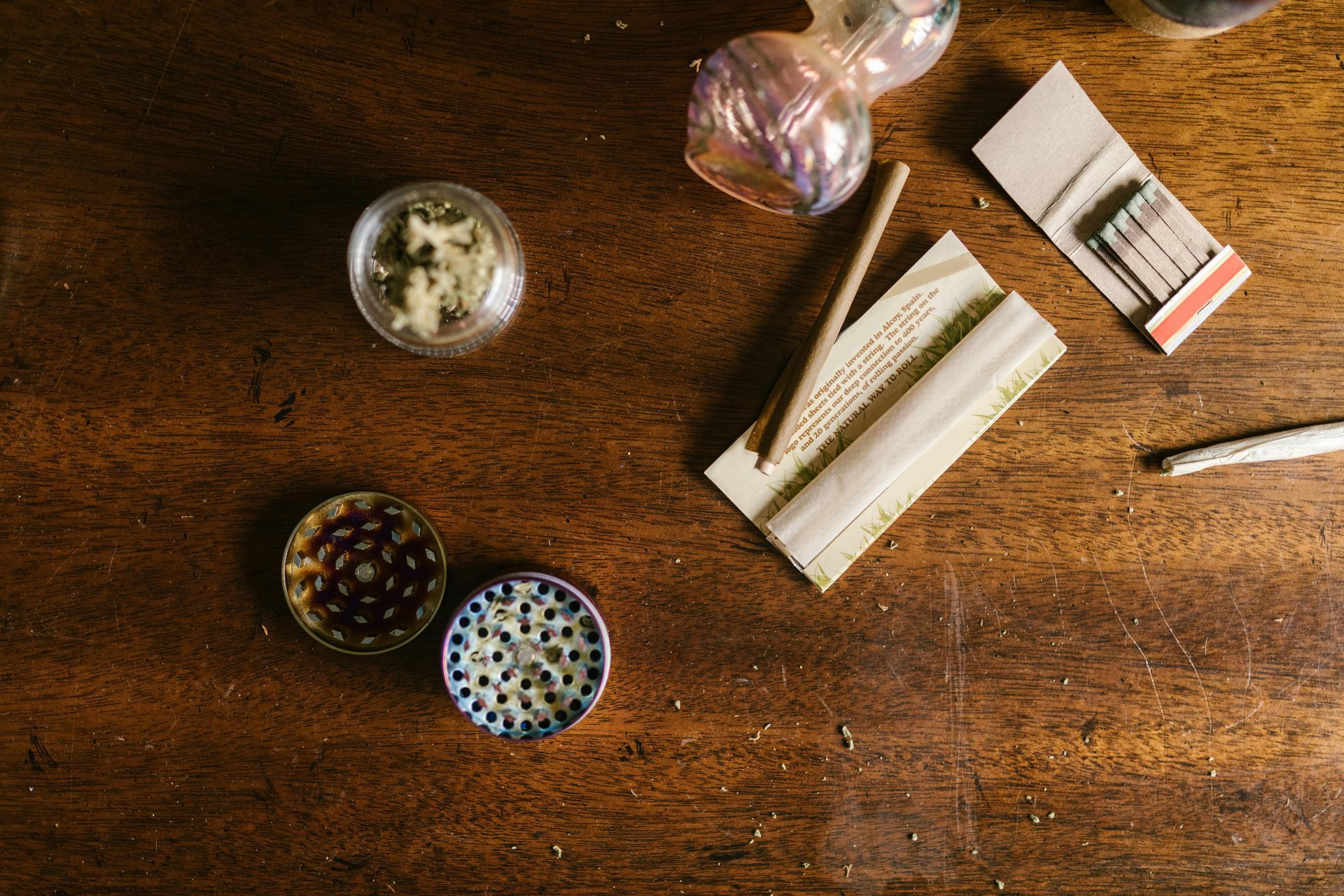Marijuana and paraphernalia on a wooden table. Includes a grinder, bud, and a rolled joint.