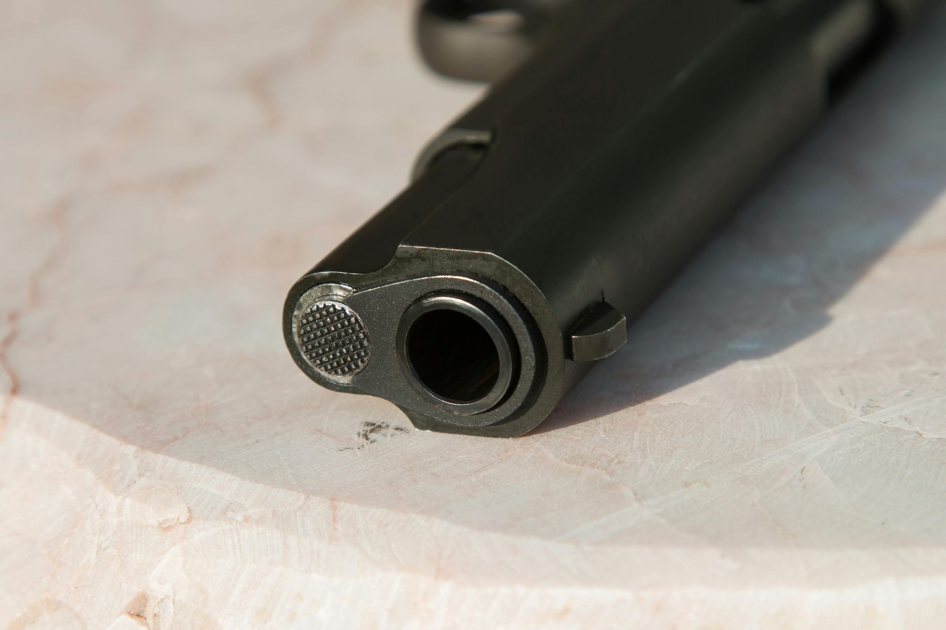 Close-up of a black handgun barrel, pointing towards the viewer on a light-colored surface.